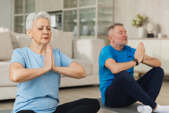Yoga mindfulness meditation. Senior adult mature couple practicing yoga at home. Mid age old husband wife sitting in lotus pose on yoga mat meditating relaxing. Family doing breathing practice