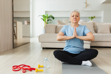 Yoga mindfulness meditation. Senior adult mature woman practicing yoga at home. Mid age old lady sitting in lotus pose on yoga mat meditating relaxing. Older middle aged woman doing breathing practice