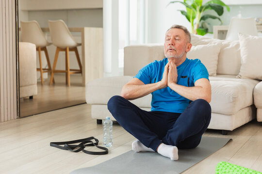 Yoga mindfulness meditation. Senior adult mature man practicing yoga at home. Mid age old grandfather sitting in lotus pose on yoga mat meditating relaxing. Older man doing breathing practice