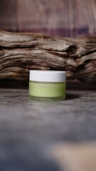 small glass jar with white cap containing light green liquid substance rests against piece of...