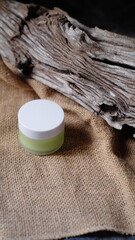 small glass jar with white cap containing light green liquid substance rests against piece of...