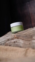 small glass jar with white cap containing light green liquid substance rests against piece of weathered wood adding natural element creating balanced aesthetic to the composition. 