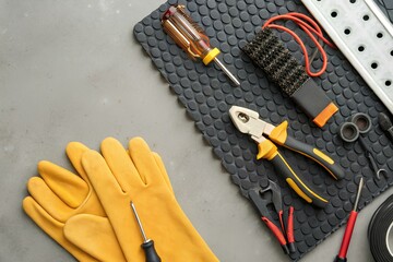 Top view of electrician tools including insulated gloves, pliers, screwdriver and wire brush arranged neatly on a textured rubber mat