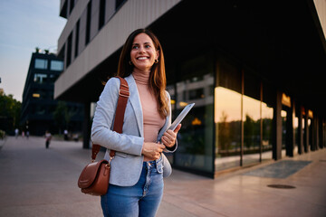 Confident Woman Holding Tablet in Modern Urban Setting During Sunset