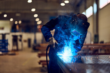 Worker Welding Metal in Industrial Workshop with Bright Sparks and Blue Light