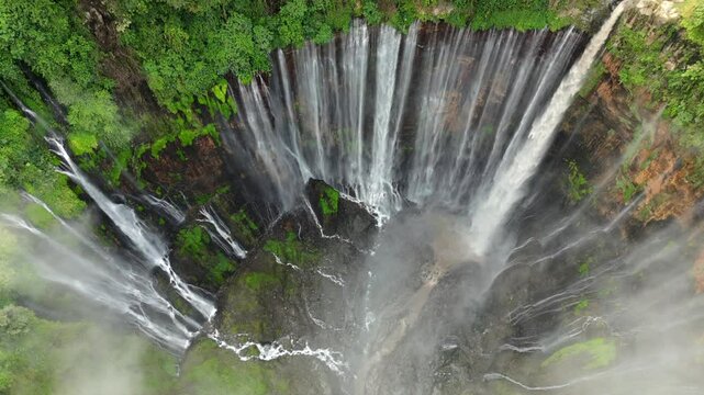Aerial view of Tumpak Sewu waterfall cascading into deep jungle canyon surrounded by lush rainforest in East Java, Indonesia.