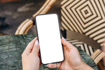 Mockup woman's hand holding using smart phone with white blank screen POV at coffee shop, mobile app design and advertising, online marketing