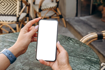Mockup woman's hand holding using smart phone with white blank screen POV at coffee shop, mobile app design and advertising, online marketing