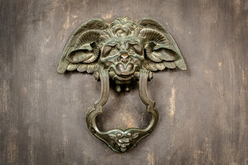 Aged bronze door knocker shaped like mythological creature on antique door