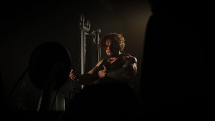 Pumped up guy doing exercises in the gym with iron, dark room, cinema light