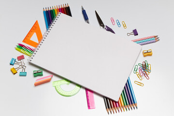 Colorful stationary and drawing supplies surround a blank sketchbook on a clean surface, creating an inviting atmosphere for art and creativity during daylight hours