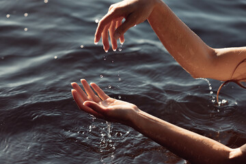 Two hands gracefully splash water in a calm lake on a sunny afternoon, creating ripples and droplets that glisten in the light. atmosphere is tranquil and refreshing