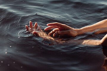 Two hands emerge from dark water, gently interacting with the surface and creating ripples. tranquil setting reflects an early evening atmosphere, enhancing the peaceful moment