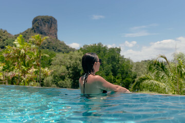 woman enjoys the calm of an infinity pool, soaking in the warm sun while overlooking a lush landscape and a prominent mountain in a tropical setting during the afternoon