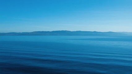 Obraz premium Calm Ocean with Distant Mountain Range Under Clear Blue Sky