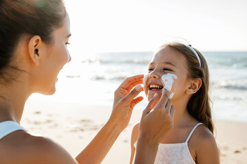 Mother applying suntan lotion on daughter face. Woman smear sunscreen or moisturizing lotion on skin. Sun cream. Skin and body care. Sun protection