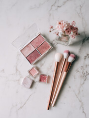 Clean and minimalistic flat lay featuring blush palette, makeup brushes, and small vase with flowers, creating serene and elegant atmosphere