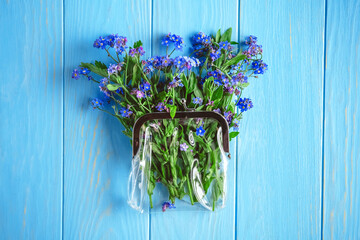 Small bouquet of forget-me-not flowers placed inside a transparent purse on a blue wooden...