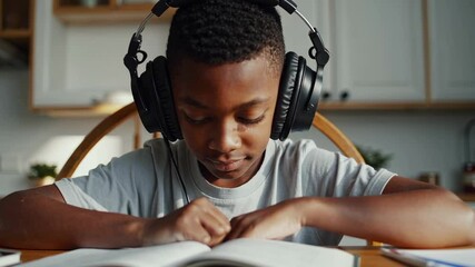 Concentrated african american boy wearing headphones is learning braille alphabet, touching book with fingers, reading and studying at home