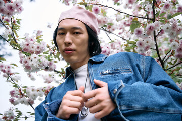 Young man embraces spring fashion in stylish denim amid blooming cherry blossoms
