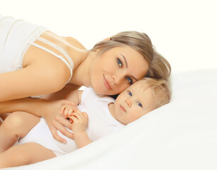 Portrait of happy young mother lying with sleepy baby together on bed at home
