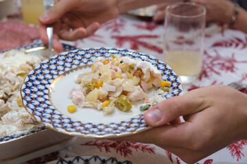 A young man serves a fresh salad from a dish at a festive table. Reflects a home feast, hospitality, healthy eating, a joyful dinner
