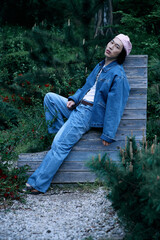 Stylish young man relaxing in a park wearing denim outfit and cap on a sunny day