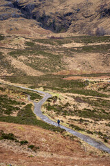 A solitary figure traverses the rugged, winding path through the majestic and mist-shrouded peaks of the Scottish Highlands, possibly in the iconic Glen Coe, where ancient landscapes meet dramatic ski