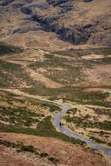 A solitary figure traverses the rugged, winding path through the majestic and mist-shrouded peaks of the Scottish Highlands, possibly in the iconic Glen Coe, where ancient landscapes meet dramatic ski