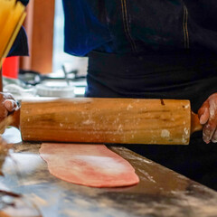  A person is rolling out dough with a wooden rolling pin on a floured kitchen counter