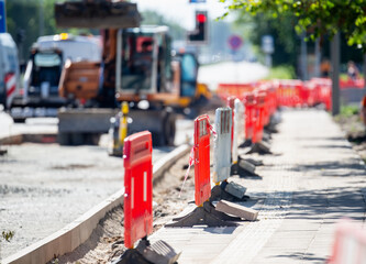 road construction site with red safety barriers and sidewalk under repair with heavy machinery and...
