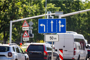urban traffic with cars at intersection under green trees and clear sky with blue directional road...