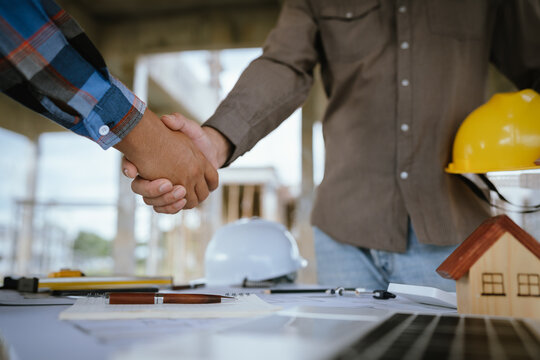 Two builders shaking hands at a construction site, representing a successful agreement and partnership built on trust, cooperation, and a shared goal of developing and growing real estate.