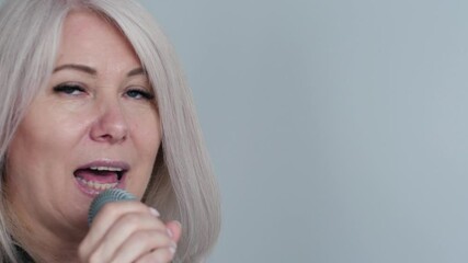 portrait of cheerful middle aged caucasian blonde woman singing song into microphone, singer rehearsing or performing song on performance, white background, concept vocal lessons