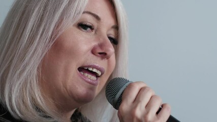 portrait of cheerful middle aged caucasian blonde woman singing song into microphone, singer rehearsing or performing song on performance, white background, concept vocal lessons