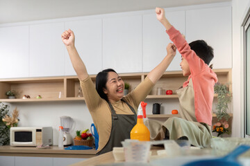 Celebrating Togetherness. Mother and son joyfully raising arms in a kitchen after completing chores.