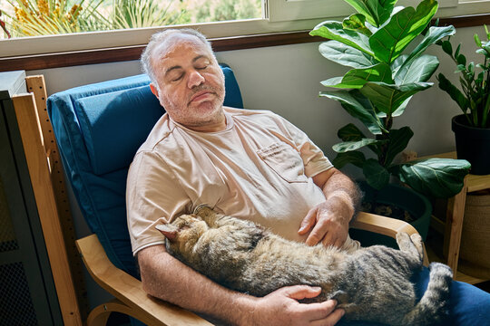 Senior man relaxing at home with a tabby cat on his lap, promoting wellbeing and affection.