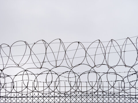 Razor wire on top of a fence against a grey sky