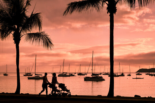 Silhouetted strollers with yachts in background at sunset on Airlie Beach.