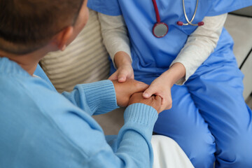 Physiotherapist attentively listens while holding elderly patient’s hands, offering comfort and...