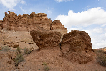 Fototapeta premium Unusual rock formations rise from the arid, rugged landscape of Charyn Canyon under a blue sky with clouds
