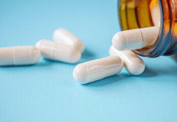 White antibiotic capsule pills spread out of pill amber glass bottle on blue background.