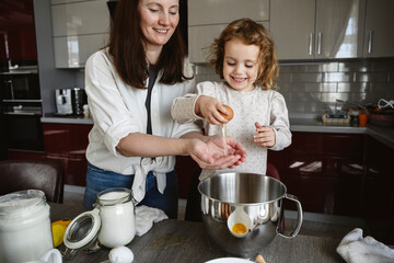Happy girl breaking egg with mother in kitchen at home