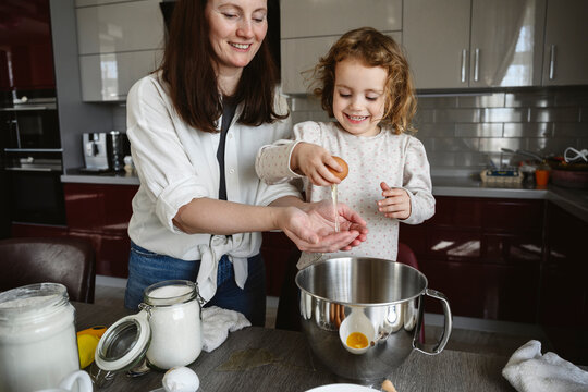 Happy girl breaking egg with mother in kitchen at home