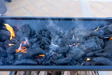 Burning charcoal embers creating smoke and flames in a barbecue grill