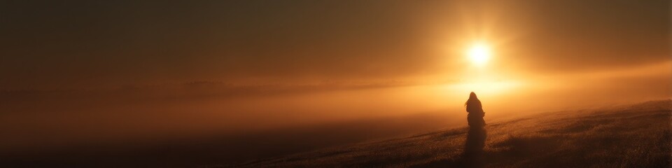 Silhouette of a person standing on a hill during a golden sunset with a hazy orange sky view
