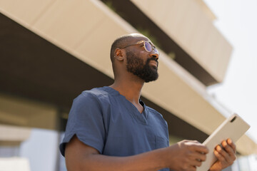 Healthcare worker in medical scrubs holding a digital tablet and looking ahead