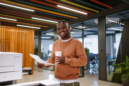 Smiling businessman holding paper and coffee in a modern office
