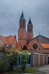 Regenwolken über und Frühlingsblüten vor der denkmalgeschützten katholischen Kirche "St. Joseph" in Luckenwalde (Ansicht von Osten)