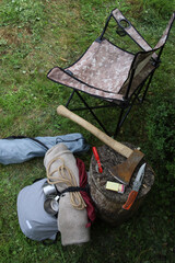 Hiking. Things and objects for tourism and survival in the forest or mountains. On the grass near the stump lie an axe, matches, canned food, rope, a tourist chair, a backpack and other things